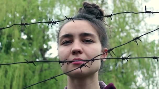 Mooi Jong Meisje Met Een Droevig Gezicht Staat Achter Prikkeldraad — Stockvideo