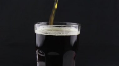 Barmen şişeden bardağa koyu bira doldurur. Bir adam bardağı koyu birayla doldurur..