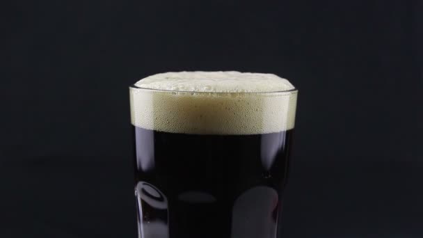 Le barman verse de la bière noire d'une bouteille dans un verre. Un homme remplit un verre de bière noire. Gros plan d'un verre de bière sombre avec de la mousse blanche sur fond noir .