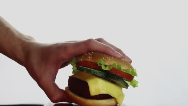 La main d'un homme prend un gros hamburger dans une assiette. Grand hamburger juteux avec escalope de bœuf, légumes frais et fromage à la crème. Les jeunes hommes main prend un hamburger d'une assiette . — Video