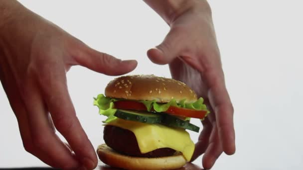 As mãos dos homens tomam um grande hambúrguer de um prato. Grande hambúrguer suculento com costeleta de carne, legumes frescos e queijo creme. Burger close-up em um fundo branco . — Vídeo de Stock