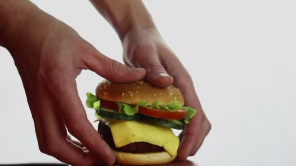 Mens χέρια λάβει ένα μεγάλο burger από ένα πιάτο. Μεγάλο ζουμερό burger με μοσχαρίσια κοτολέτα, φρέσκα λαχανικά και τυρί κρέμα. Burger close-up σε λευκό φόντο. — Αρχείο Βίντεο