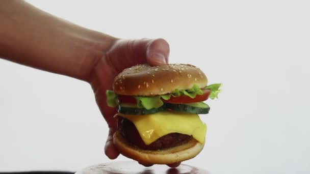 La main d'un homme prend un gros hamburger dans une assiette. Grand hamburger juteux avec escalope de bœuf, légumes frais et fromage à la crème. Les jeunes hommes main prend un hamburger d'une assiette . — Video