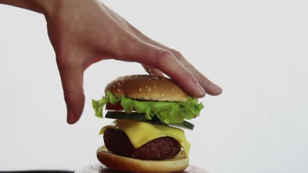 男性の手は 材料を示すバーガーを伸ばし 大きなバーガーの構成 成分は 個別に空気中にハングアップ バーガーの構成部分 ファーストフード 高カロリー食品 白を基調としたバーガークローズアップ — ストック動画