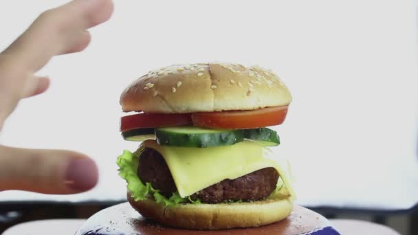 Kadın eli tabaktan büyük bir hamburger alır. Sığır pirzolası, taze sebze ve krem peynirli büyük sulu burger. Genç bir kızın eli tabaktan bir hamburger alır.. — Stok video