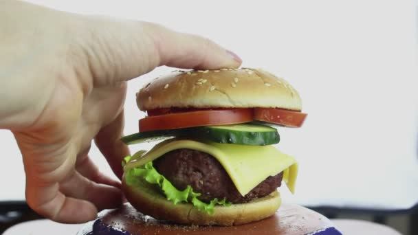 La main féminine prend un gros hamburger dans une assiette. Grand hamburger juteux avec escalope de bœuf, légumes frais et fromage à la crème. La main d'une jeune fille prend un hamburger dans une assiette . — Video