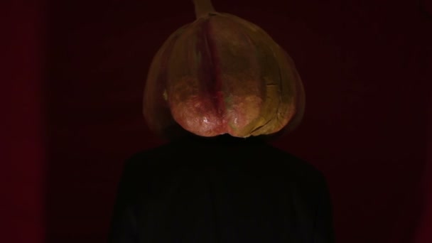 Scary man with a pumpkin head and luminous eyes looks at the camera. Man with a pumpkin head scares raising his hands up. Halloween. — Stock video