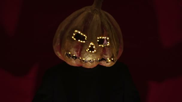 Homme effrayant avec une tête de citrouille et les yeux lumineux regarde la caméra. L'homme à la tête de citrouille a peur de lever les mains. Halloween . — Video