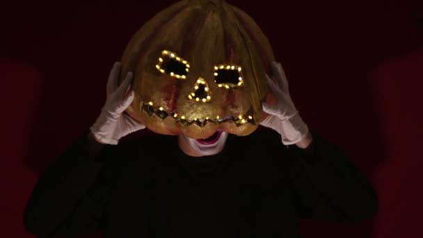 Scary man in the makeup of a clown holds a pumpkin for Halloween and puts it on his head.Terrible clown puts on a mask in the shape of a pumpkin on his head. Terrible clown holds in his hands a Jack-O — 图库视频影像