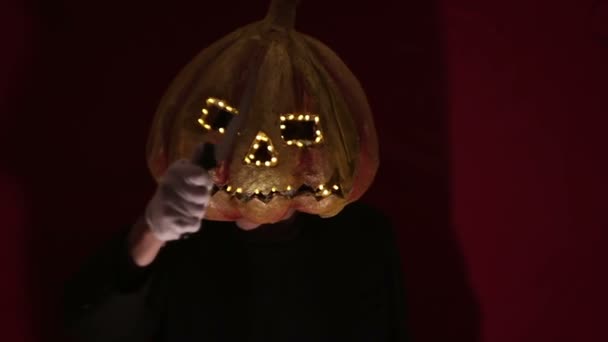 Uomo spaventoso con la testa di zucca e gli occhi luminosi guarda la fotocamera. L'uomo con la testa di zucca ha paura di alzare le mani. Halloween . — Video Stock