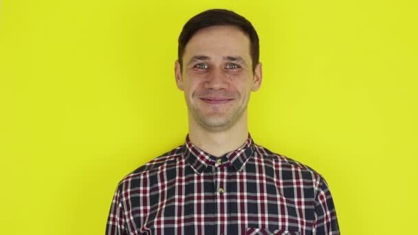 Closeup portrait of a young attractive guy, he is looking at the camera and smiling. Portrait on a yellow background. — Stock Video