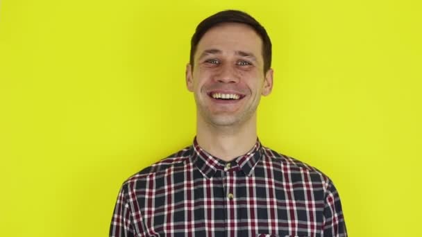 A young handsome guy in a plaid shirt, looks at the camera and expressively laughs. Portrait on a yellow background. — Stock Video