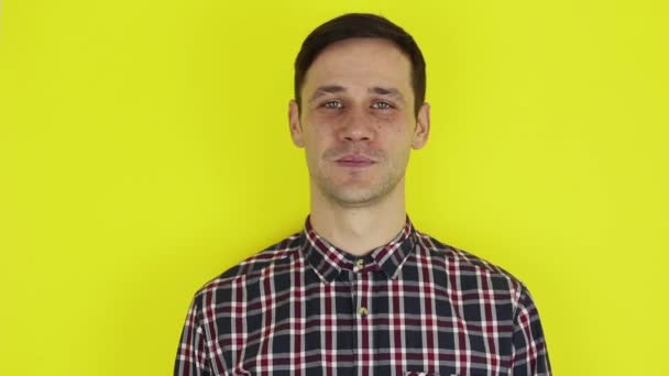 A young handsome guy in a plaid shirt, looks at the camera and expressively laughs. Portrait on a yellow background. — Stock Video