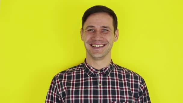 Close-up portrait of a young attractive guy, he laughs and looks at the camera. Portrait on a yellow background. — Stok video