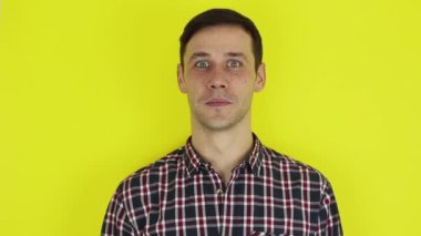 Close up portrait of a young attractive guy, he smiles and waves his hand in greeting to his friends. . Portrait on a yellow background.
