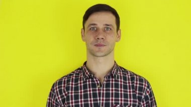 Young handsome guy in a plaid shirt, looking at the camera, smiling and waving his hand in greeting .