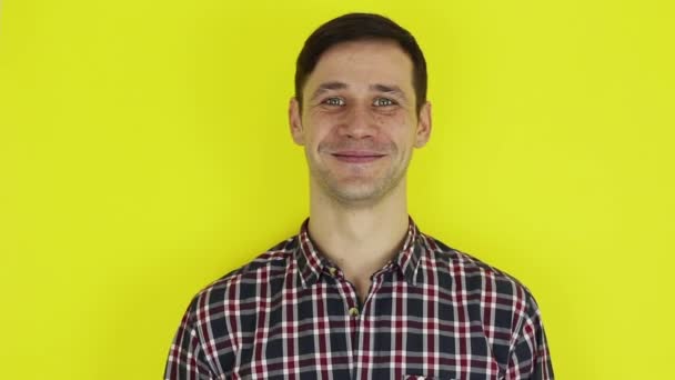 Close up portrait of a young attractive guy, he is smiling and waving goodbye to his friends. Portrait on a yellow background. — Stockvideo