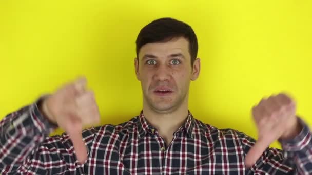 Funny handsome guy says the word badly and shows thumb down with both hands. Portrait on a yellow background. — Stock Video