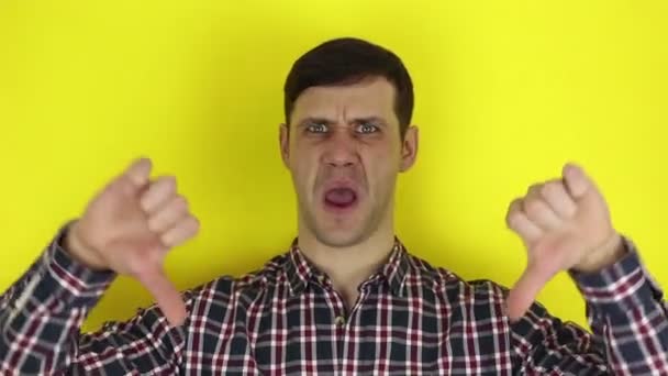 Funny handsome guy says the word badly and shows thumb down with both hands. Portrait on a yellow background. — Stock Video