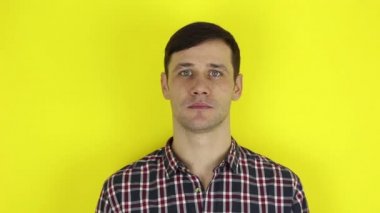 A funny handsome guy says no and shakes his head negatively. Portrait on a yellow background.