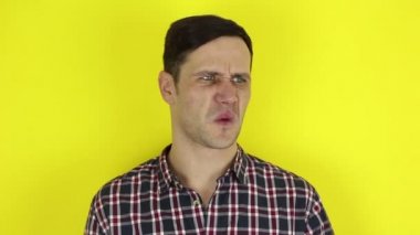 Komik, sevimli bir adam havayı kokluyor ve eliyle burnunu kapatıyor. Genç bir adamın portresi, kötü hava kokmasın diye burnunu parmaklarıyla kapatır. Sarı arka plandaki portre..