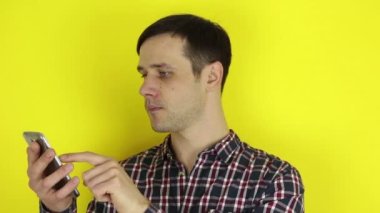 Komik, sevimli bir adam akıllı telefonuyla sosyal medyayı kurcalıyor. Genç bir adamın portresi, akıllı telefonuyla sosyal medyayı aktif olarak izliyor. Sarı arkaplanda bir portre.
