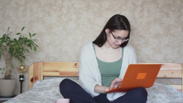 年轻迷人的女孩在家里坐在床上时 做着远程工作 年轻可爱的女孩坐在床上 在笔记本电脑前工作 在家工作 — 图库视频影像