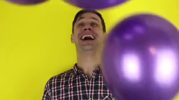 面白い かわいい男が積極的に紫色の風船で遊んでいます 紫色の風船で楽しさと遊びを積極的に表現した若い男の肖像画 美しい男は風船で遊んで誕生日を祝う 黄色の背景の肖像画 — ストック動画