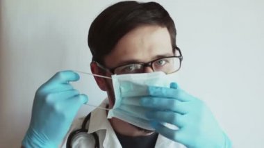 Genç yakışıklı doktor hastaları muayene etmek için tıbbi maske takıyor. Genç bir doktor bir hastayı muayene etmeye hazırlanıyor..