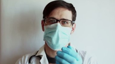 Genç, yakışıklı bir doktor eldivenlerini çıkardı, tıbbi maskesini çıkardı ve rahatça iç çekti. Genç bir doktor, yorucu bir günün ardından tıbbi maskesini çıkarıyor..