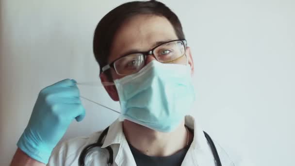 若いハンサムな医者は彼の医療保護マスクを脱いで 重くため息をつく 若い医者は一日の仕事の後に医療マスクを削除します — ストック動画