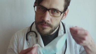 Genç yakışıklı doktor hastaları muayene etmek için tıbbi maske takıyor. Genç bir doktor bir hastayı muayene etmeye hazırlanıyor..