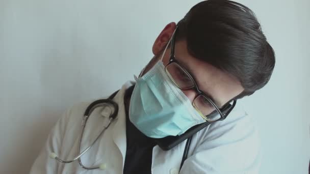 眼鏡をかけた若いハンサムな医者と医療面のマスクは 電話で相談を与えます 若い医者は隔離中に電話で患者に相談する — ストック動画