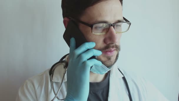 一位戴着眼镜和医疗面罩的年轻貌美的医生在电话里提供咨询 — 图库视频影像