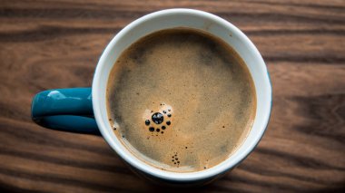 Ahşap bir masanın üzerinde bir fincan aromatik kahve duruyor. Köpüklü Aromatik kahve. Lezzetli süt köpüklü canlandırıcı kahve.