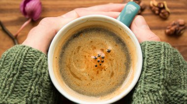 Bir erkek eli bir fincan aromatik kahve tutuyor. Ahşap bir masanın üzerinde bir fincan aromatik kahve duruyor. Bir adam bir fincan kahveyle ellerini ısıtır..