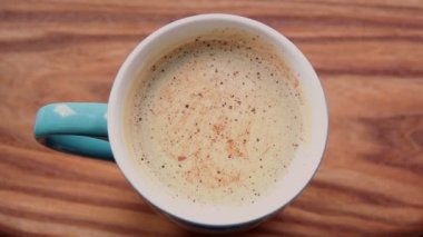 Bir erkek eli bir fincan aromatik kahve tutuyor. Ahşap bir masanın üzerinde bir fincan aromatik kahve duruyor. Bir adam bir fincan kahveyle ellerini ısıtır. Lezzetli süt köpüklü canlandırıcı kahve.