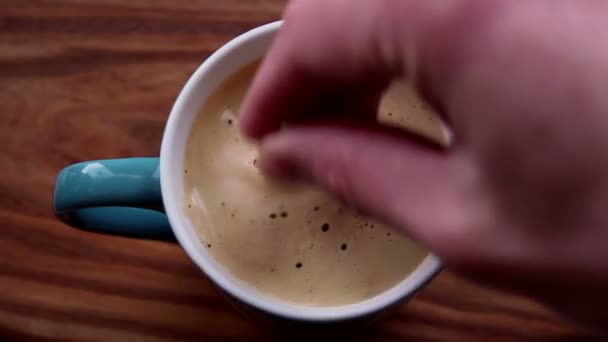 Un homme mélange du sucre dans une tasse de café aromatique. Une tasse de café aromatique est placée sur une table en bois. Les mains de l'homme remuent une boisson au café avec une cuillère. Café revigorant avec une délicieuse mousse de lait .