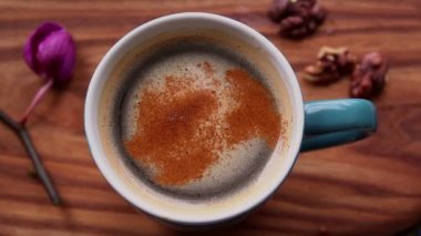 Bir adam bir fincan aromatik kahveye baharat ekler. Ahşap bir masanın üzerinde bir fincan aromatik kahve duruyor. Erkek eli, kahve içeceğine tarçın ekler. Lezzetli süt köpüklü canlandırıcı kahve.