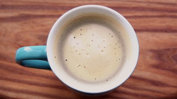 一杯香浓的咖啡站在一张木制桌子上 带有泡沫的芳香咖啡 用美味的牛奶泡沫加满咖啡 牛奶泡沫在一杯咖啡中旋转 — 图库视频影像
