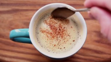 Bir adam bir fincan aromatik kahvenin içinde şeker karıştırır. Bir fincan aromatik kahve ahşap bir masanın üzerine konur. Erkek eli kaşıkla kahve içmeyi karıştırır. Lezzetli süt köpüklü canlandırıcı kahve.