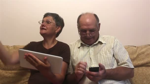 魅力的な大人の女性と大人の男性は タブレットPc上で家族とビデオ通話を行います 高齢者のカップルは 自宅でソファに座って タブレット上でビデオ通話を行います — ストック動画