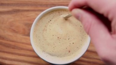 Bir adam bir fincan aromatik kahveye şeker karıştırır. Ahşap bir masanın üzerinde bir fincan aromatik kahve duruyor. Erkekler kaşıkla kahve içmeyi karıştırır..