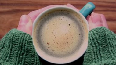Bir erkeğin elleri bir fincan aromatik kahve tutuyor. Ahşap bir masanın üzerinde bir fincan aromatik kahve duruyor. Bir adam bir fincan kahveyle ellerini ısıtır..