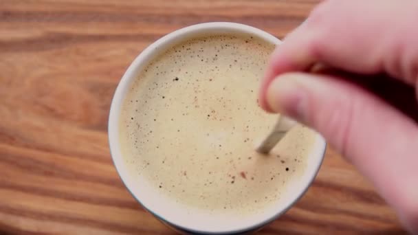 En man rör socker i en kopp aromatiskt kaffe. En kopp aromatiskt kaffe placeras på ett träbord. Man händer rör en kaffe dryck med en sked. — Stockvideo