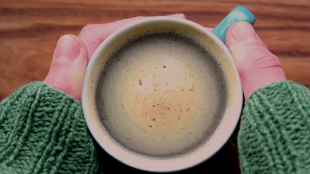 Un uomo mani sono in possesso di una tazza di caffè aromatico. Una tazza di caffè aromatico poggia su un tavolo di legno. Un uomo si scalda le mani con una tazza di caffè . — Video Stock