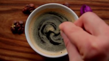 Bir adam bir fincan aromatik kahvenin içinde şeker karıştırır. Bir fincan aromatik kahve ahşap bir masanın üzerine konur. Erkek eli kaşıkla kahve içmeyi karıştırır..