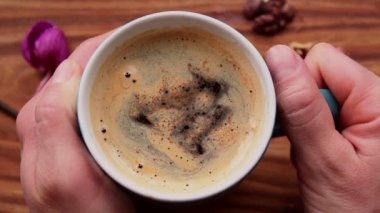 Kadın eli, aromatik kahve bardağını tutar. Ahşap bir masanın üzerinde bir fincan aromatik kahve duruyor. Lezzetli süt köpüklü canlandırıcı kahve.