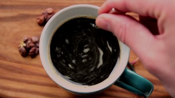 Egy férfi cukrot kever egy csésze aromás kávéba. Egy csésze aromás kávé kerül egy fa asztalra. A férfi keze egy kanállal keveri a kávét.. — Stock videók
