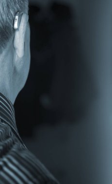 Kafkasyalı beyaz yaşlı adam kulağına modern dijital işitme cihazı takıyor ve gri saçlı..